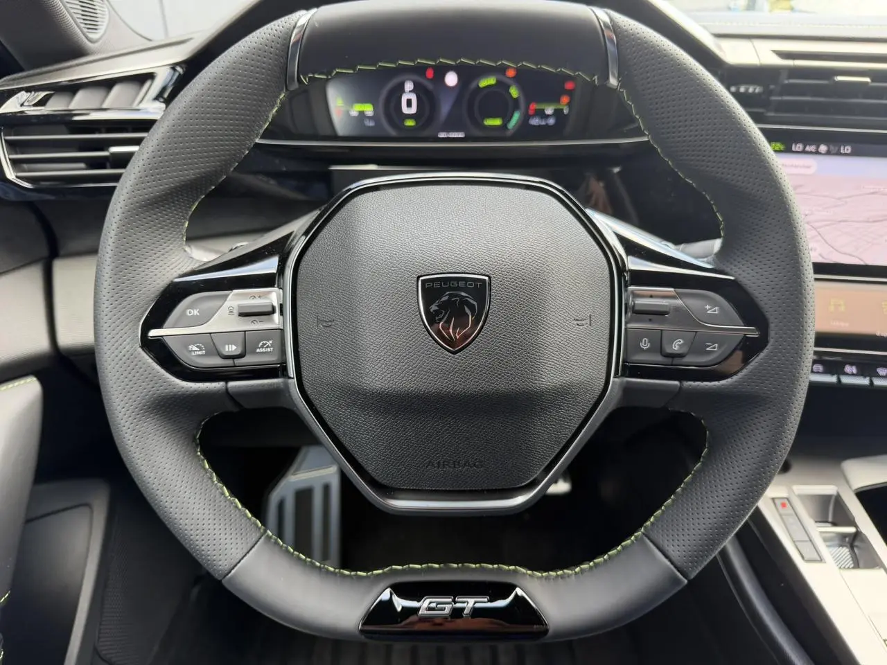 Vue rapprochée du volant compact GT en cuir noir avec surpiqûres vert Adamite et logo Peugeot au centre.