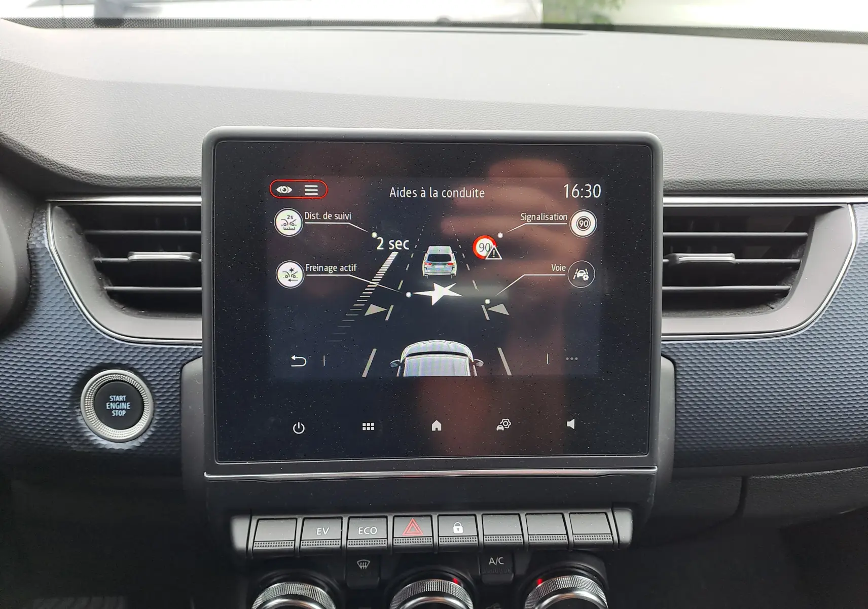 Écran central du tableau de bord du Renault Arkana 2023 affichant les aides à la conduite, avec boutons de commande en dessous.