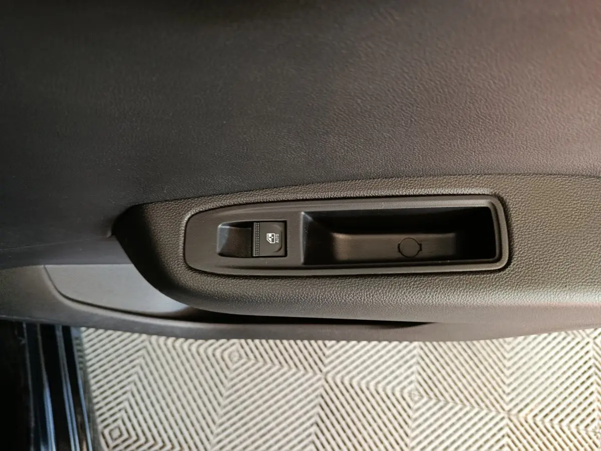 Gros plan sur la commande de lève-vitre électrique côté gauche de la porte intérieure noire d'une Renault Clio 2025.