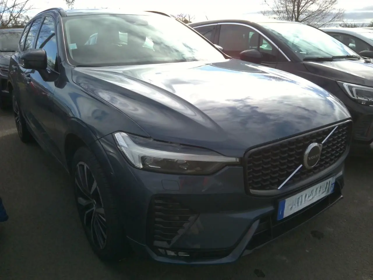 Vue 3/4 avant droite d'un Volvo XC60 bleu avec calandre noire laquée et jantes alliage 20 pouces bicolores.