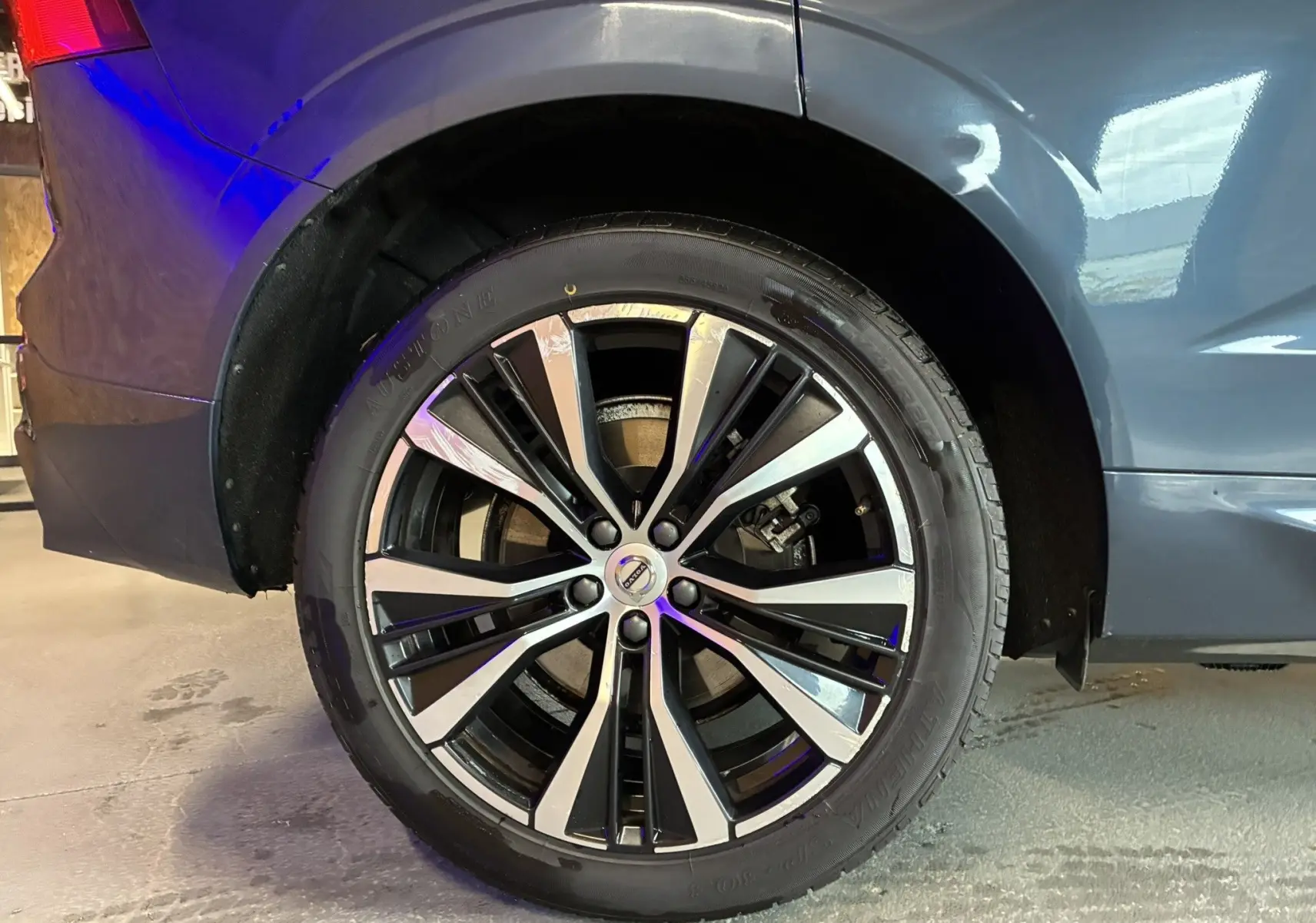 Gros plan sur la roue arrière droite du Volvo XC60 bleu 2023 avec jante alliage 20'' noir et diamant.