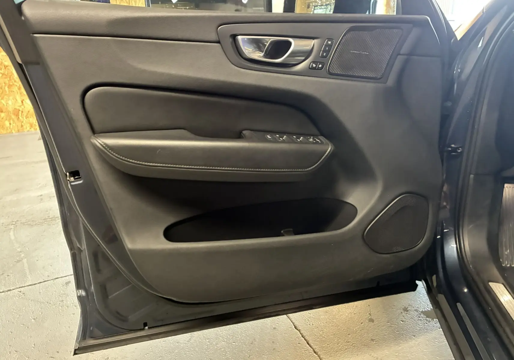 Vue intérieure de la porte avant gauche du Volvo XC60 bleu 2023 avec garniture noire et haut-parleur Harman Kardon.