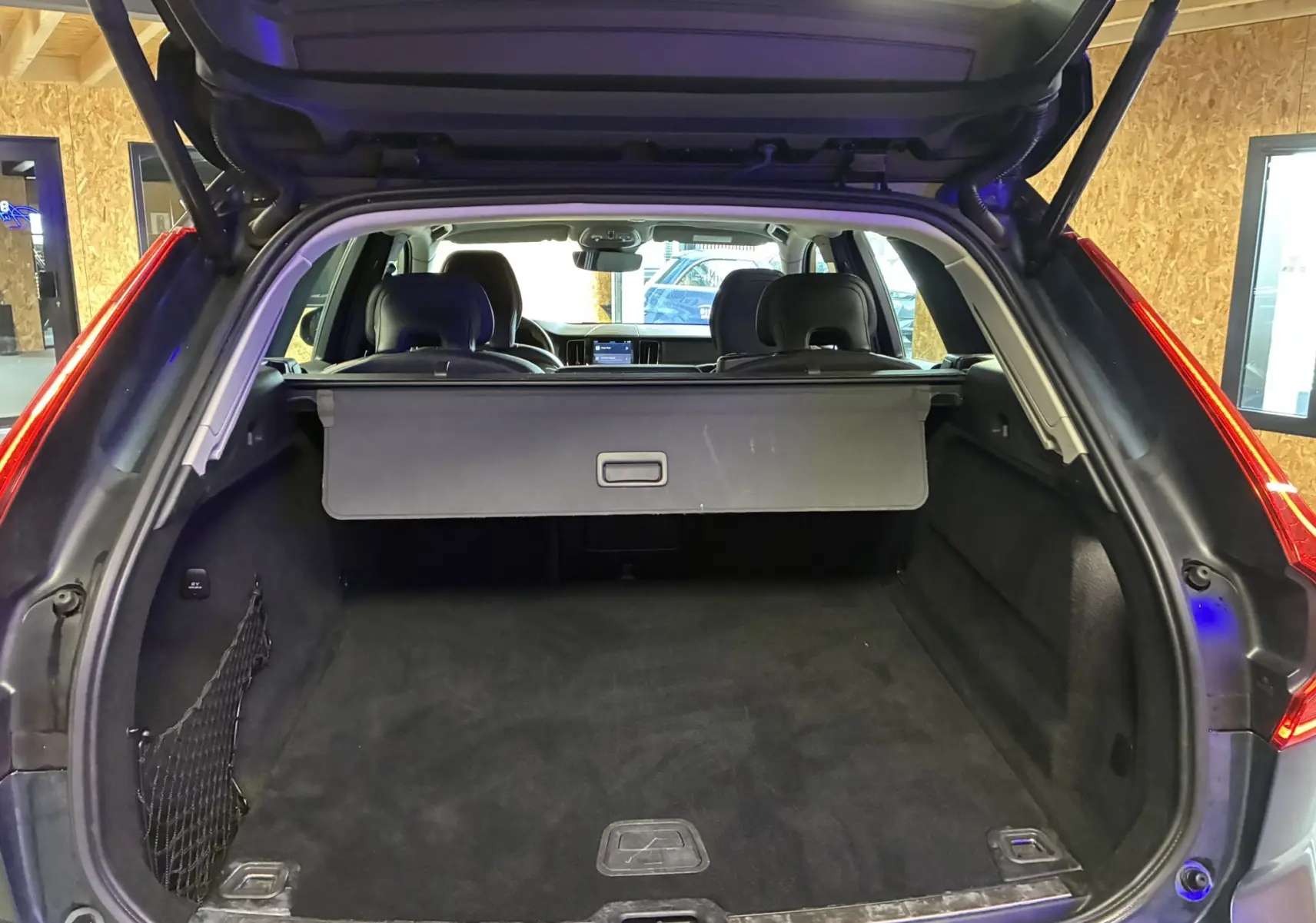 Coffre ouvert vu de l'arrière d'un Volvo XC60 bleu, montrant l'espace de chargement et la plage arrière.
