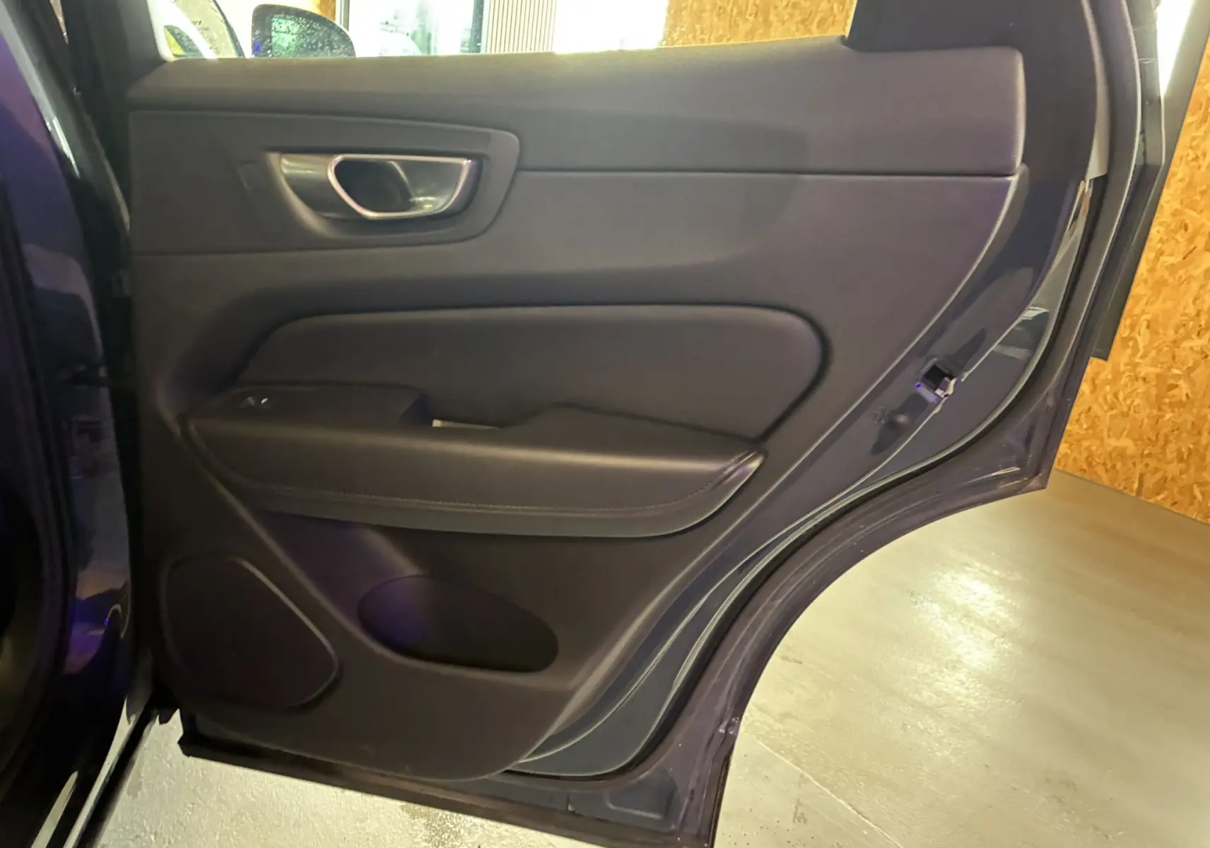 Vue intérieure de la porte arrière gauche bleu foncé du Volvo XC60 2023 avec garniture noire et poignée argentée.