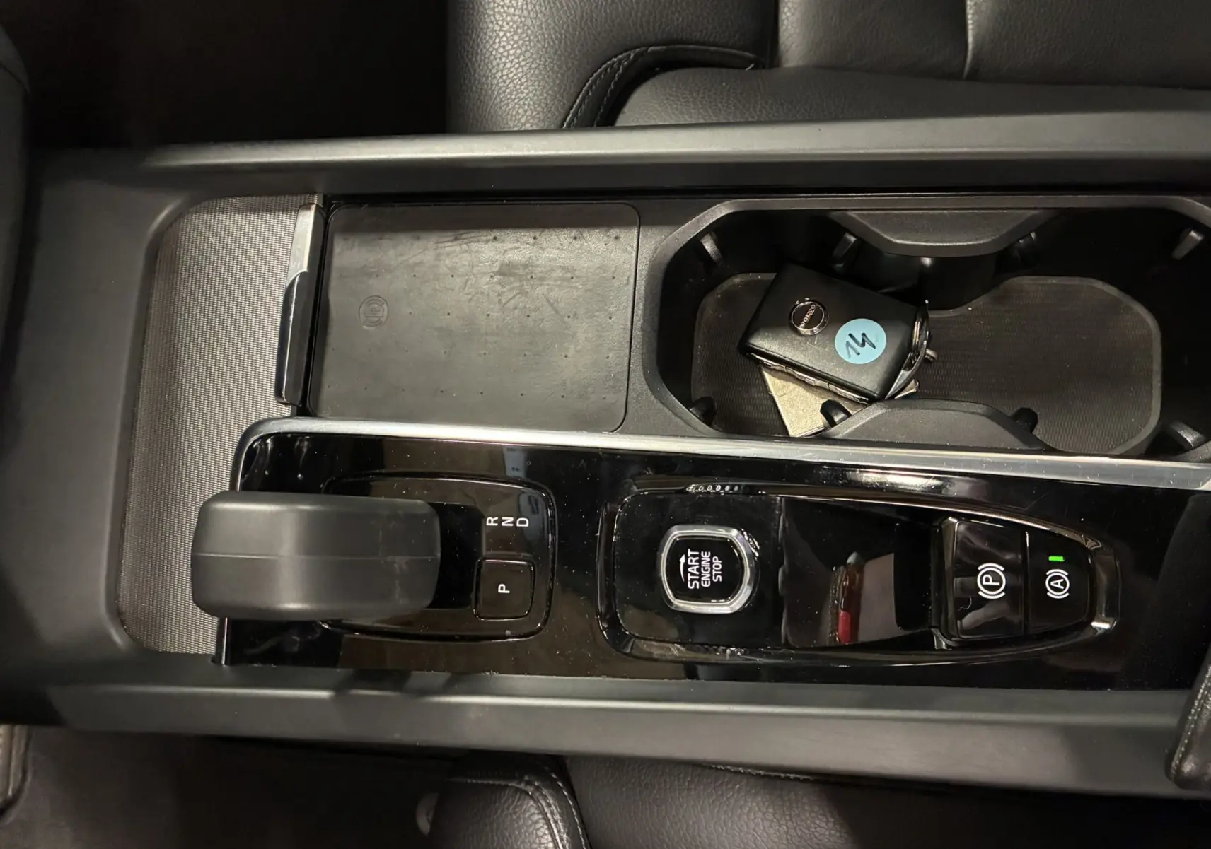 Vue plongeante sur la console centrale noire brillante du Volvo XC60 avec levier de vitesse et clé dans porte-gobelets.