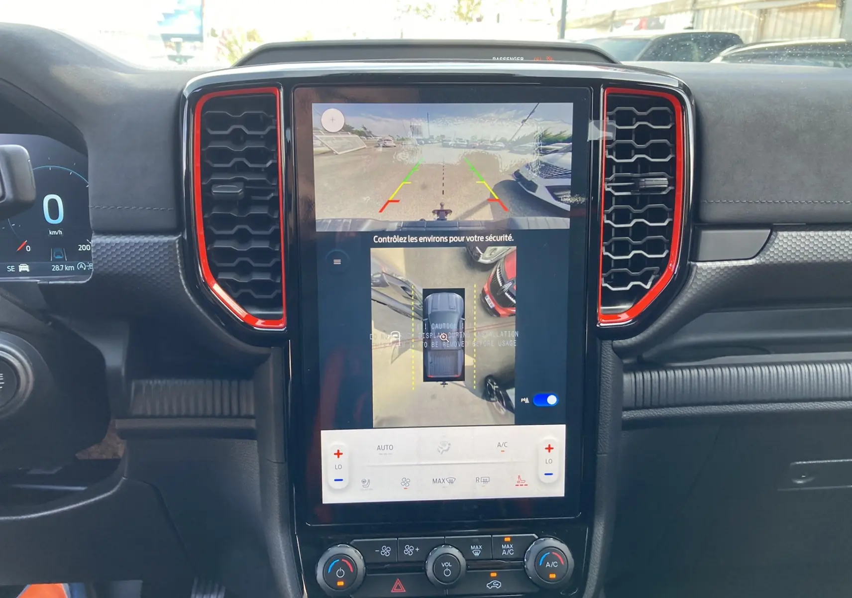 Vue intérieure centrée sur l’écran tactile vertical du Ford Ranger Raptor 2026 avec cadre rouge et commandes climatisation.