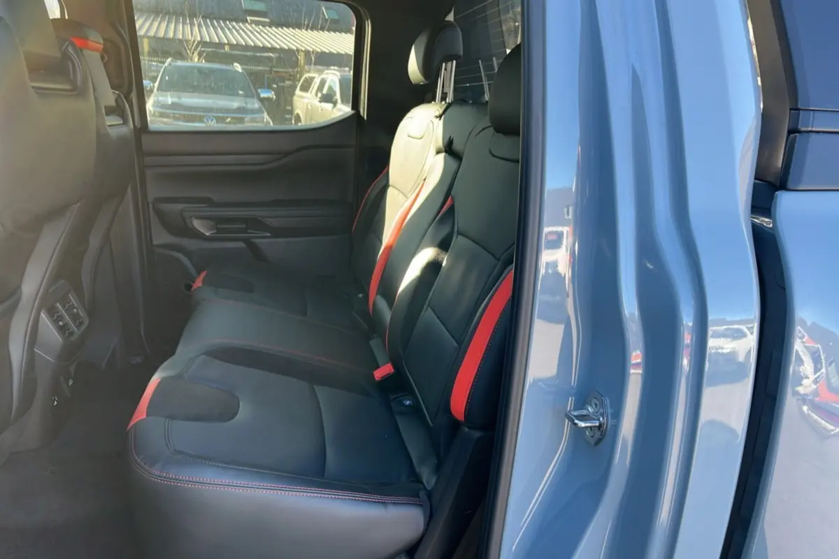 Vue intérieure arrière côté droit du Ford Ranger Raptor 2026 gris commandeur, sièges cuir noirs avec surpiqûres rouges.