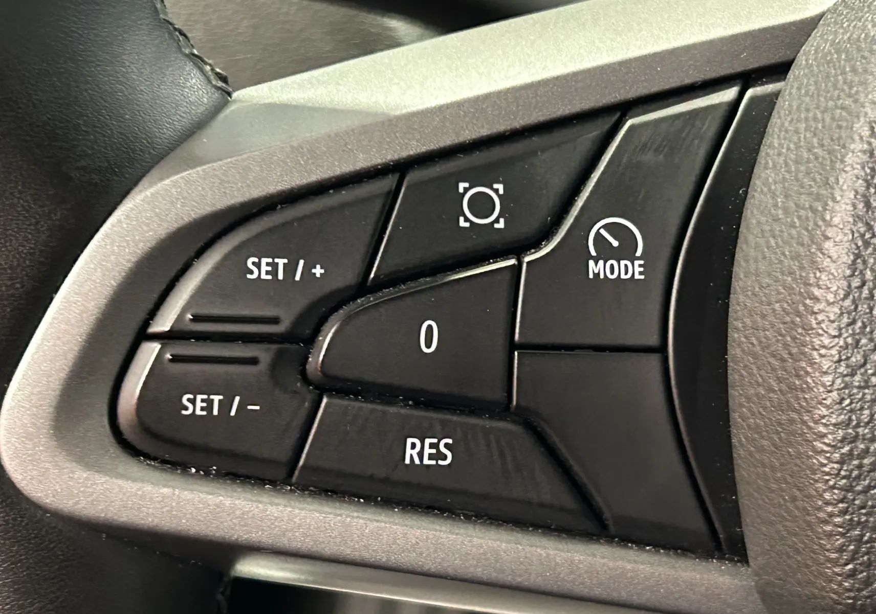 Gros plan sur les commandes noires du volant du Dacia Duster 2024, boutons de réglage et mode visibles.