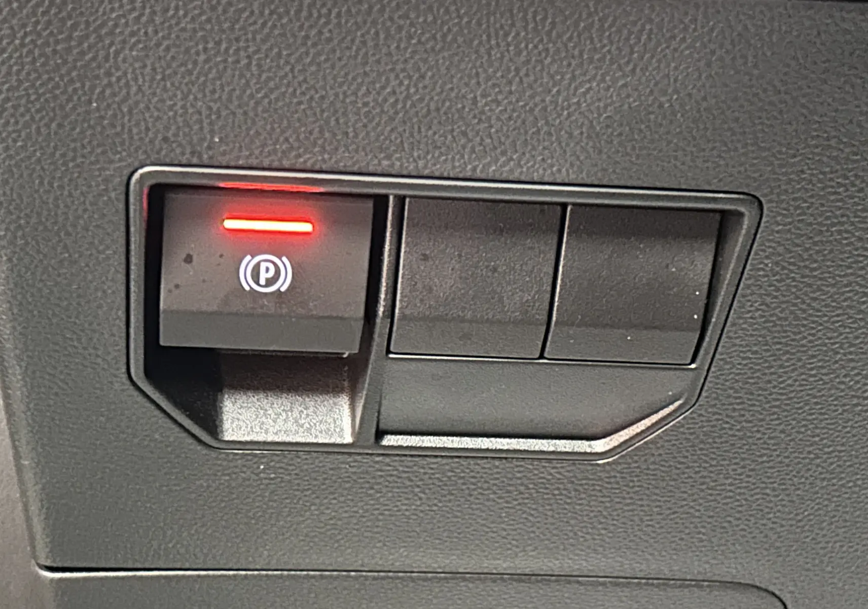 Gros plan sur le bouton de frein à main électronique allumé dans l’habitacle du Dacia Duster 2024 couleur Sandstone.