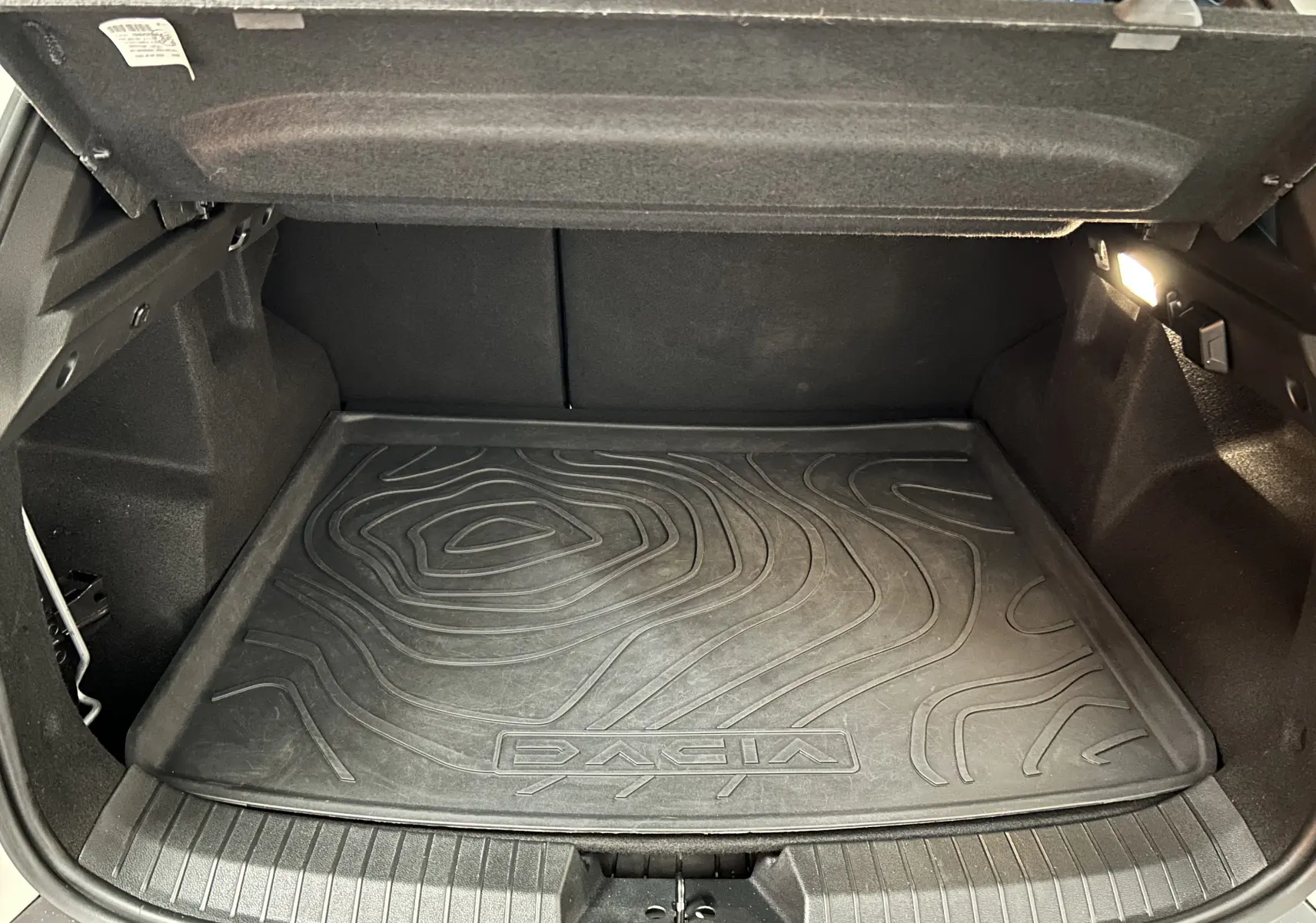 Coffre ouvert du Dacia Duster 2024 avec tapis de sol noir texturé et éclairage intérieur à droite.