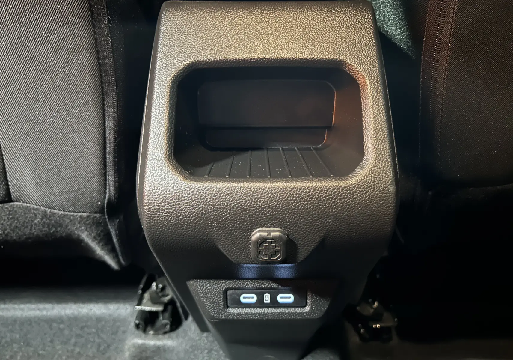 Gros plan sur la console arrière noire du Dacia Duster 2024 avec prises USB-C et rangement intégré.