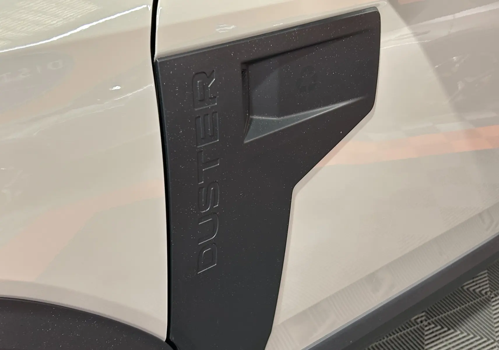 Gros plan sur l’écusson noir « DUSTER » sur la carrosserie beige sandstone du SUV Dacia Duster 2024.
