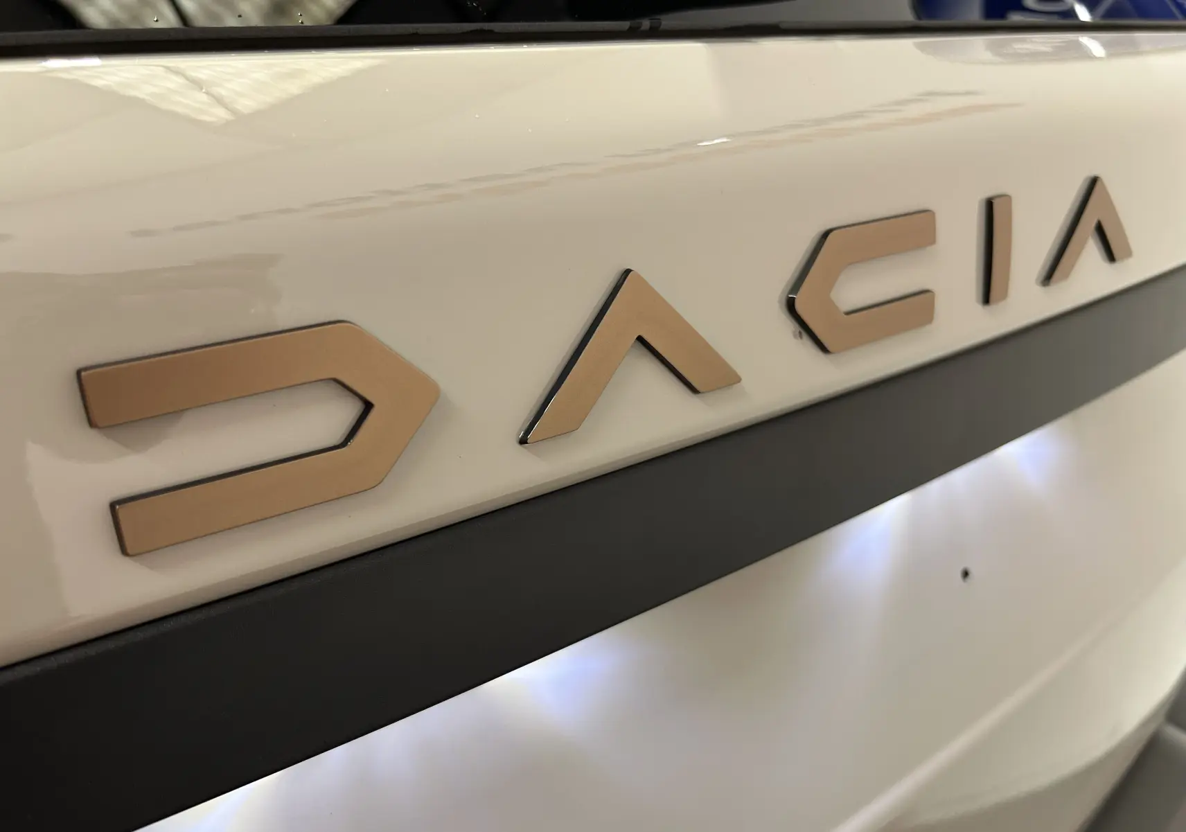 Gros plan sur le logo DACIA en relief couleur sable sur la porte arrière blanche du Duster 2024.