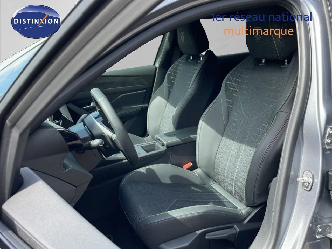 Vue intérieure côté conducteur de la Peugeot 308 gris Artense, sièges en tissu noir avec surpiqûres grises et volant cuir multifonction.