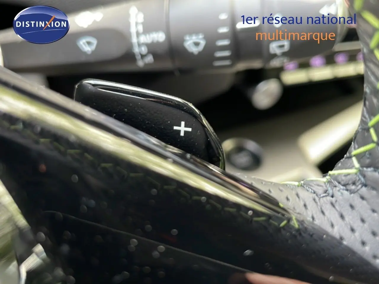 Gros plan sur la palette de changement de vitesse + du volant cuir noir avec surpiqûres vertes d'une Peugeot 308 gris Artense.