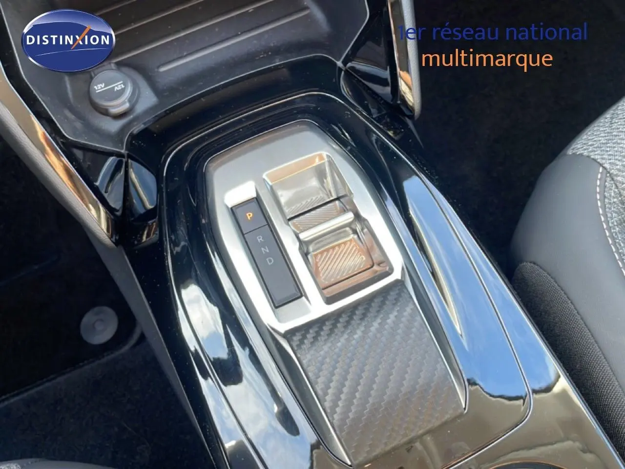 Gros plan sur la console centrale noire brillante de la Peugeot 208 Hybrid 110ch, avec levier de boîte automatique et finition carbone.