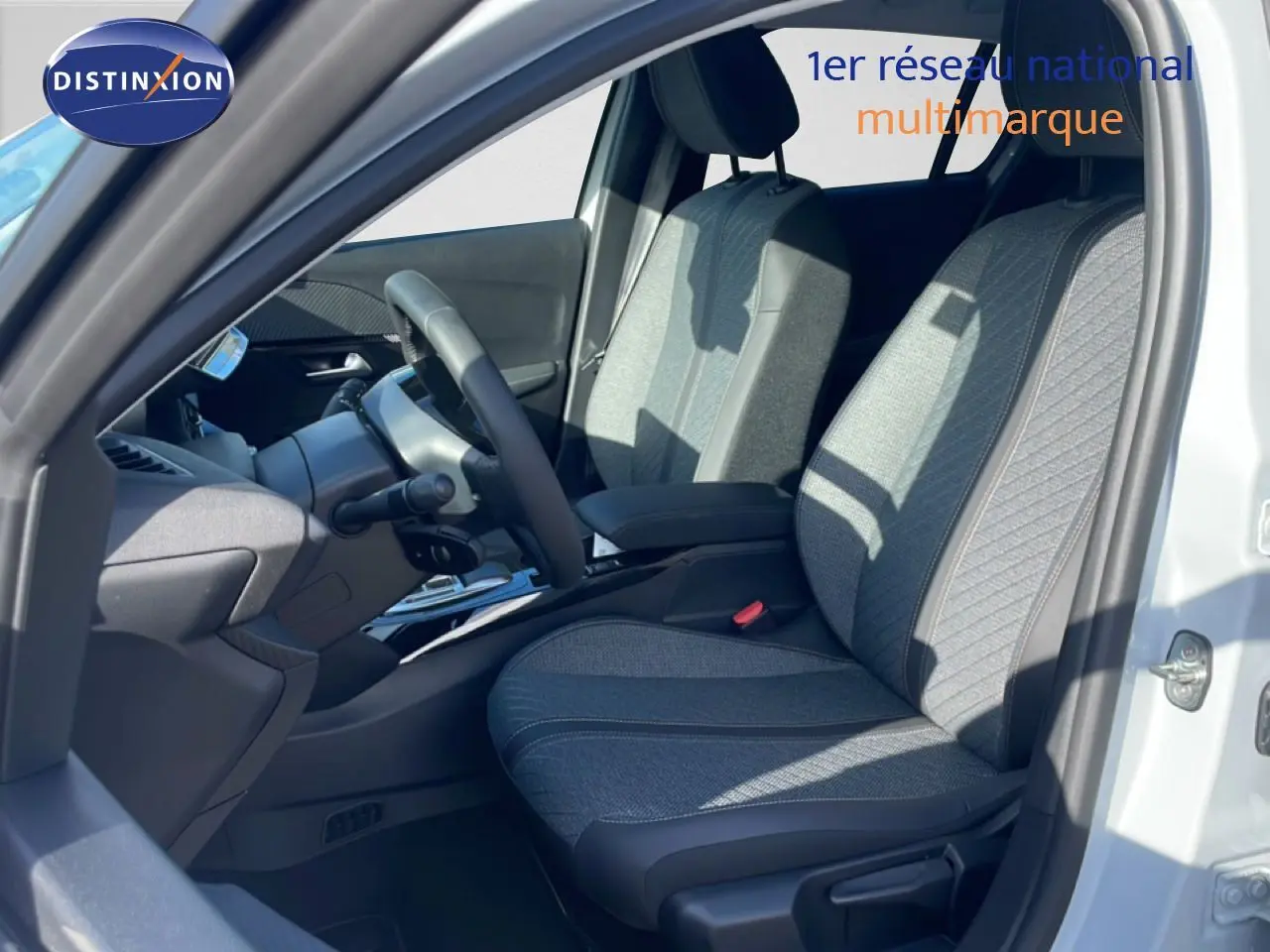 Vue intérieure côté conducteur de la Peugeot 208 Hybrid blanche, montrant les sièges en tissu gris et le volant multifonction.