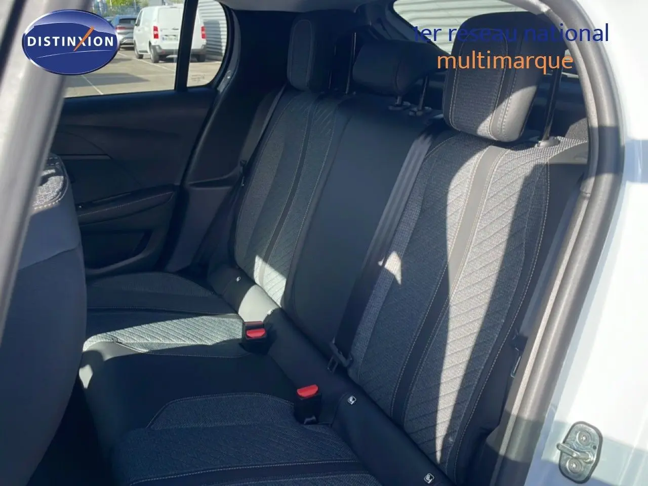 Vue intérieure côté droit montrant la banquette arrière en tissu gris avec surpiqûres, porte ouverte d'une Peugeot 208 blanche.