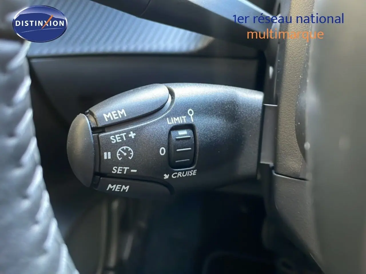 Gros plan sur la commande de régulateur de vitesse à gauche du volant dans une Peugeot 208 blanche hybride 2026.