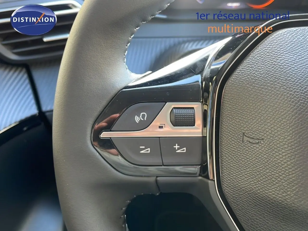 Gros plan sur les commandes gauche du volant cuir noir d’une Peugeot 208 Hybrid blanche, avec boutons de volume et de commande vocale.