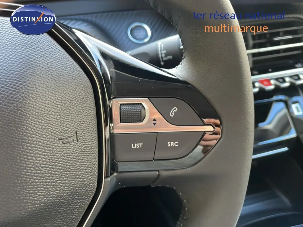Gros plan sur les commandes gauche du volant cuir noir d’une Peugeot 208 Hybrid blanche, avec tableau de bord en arrière-plan.