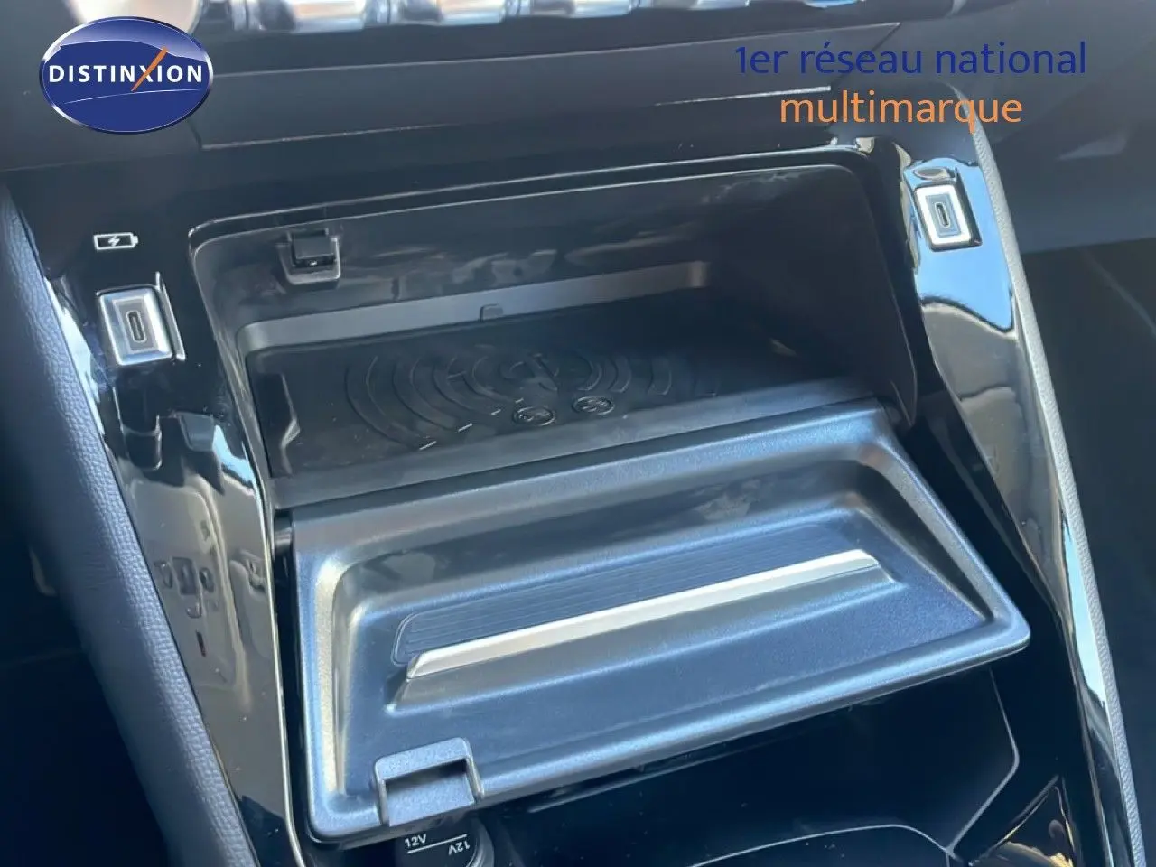 Gros plan sur la console centrale noire brillante de la Peugeot 208 Hybrid 110ch avec compartiment ouvert et prises USB visibles.