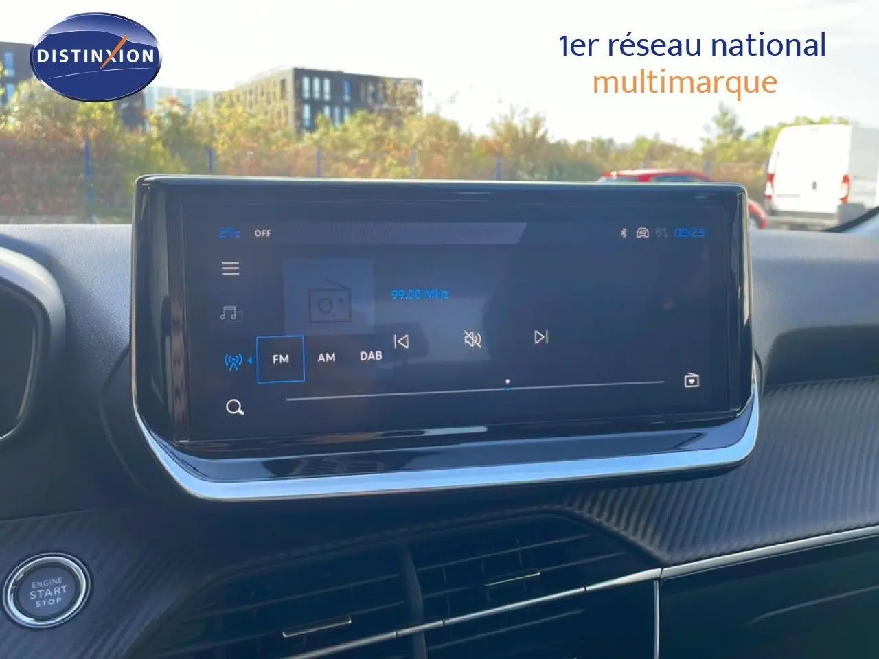 Écran tactile central du tableau de bord d’une Peugeot 208 hybride blanche, affichant la radio FM à 99 MHz.