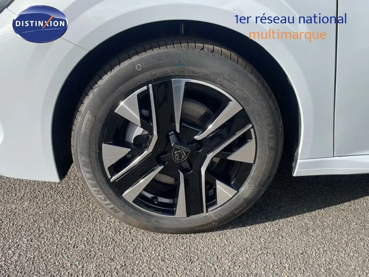 Gros plan sur la roue avant gauche d’une Peugeot 208 blanche, jante alliage noire et argentée au design moderne.