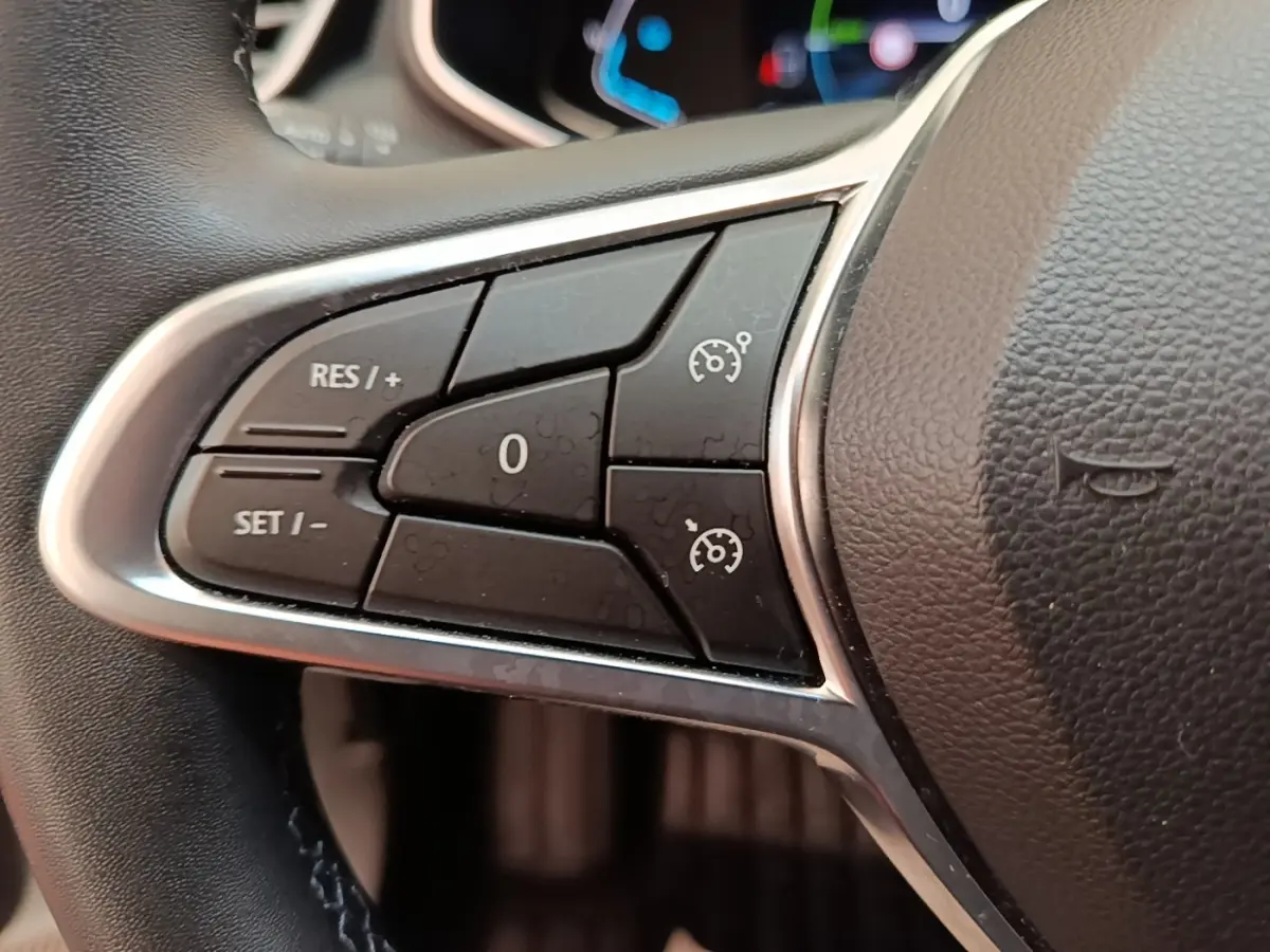 Gros plan sur les commandes du régulateur de vitesse du volant en cuir synthétique d'une Renault Clio Business E-TECH 140 blanche.