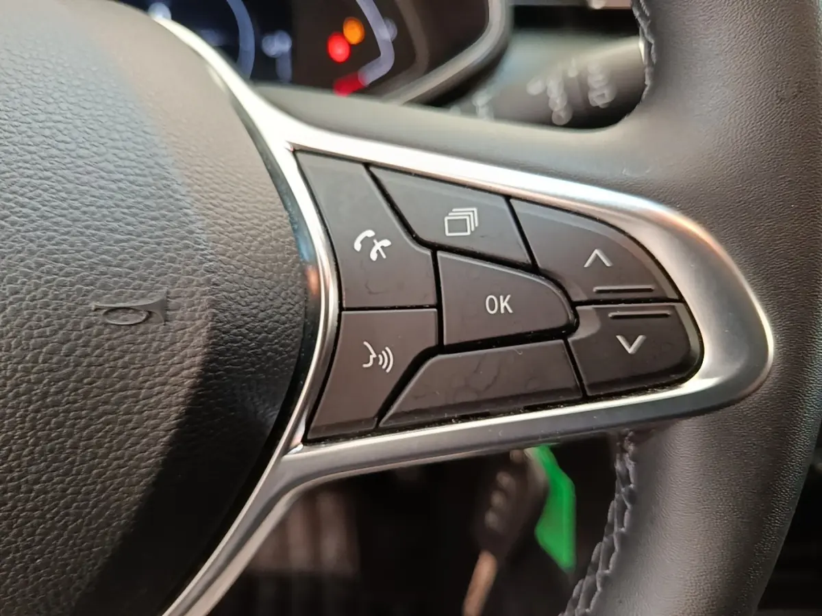 Gros plan sur les commandes multifonctions à droite du volant cuir synthétique de la Renault Clio Business E-TECH 140 blanche.