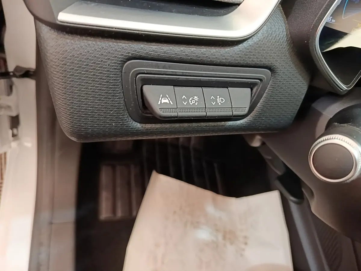 Gros plan sur les commandes d’aide à la conduite sous le tableau de bord d’une Renault Clio blanche, côté conducteur.