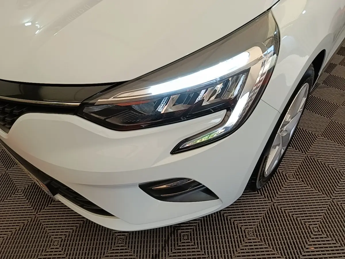 Gros plan sur l'avant droit de la Renault Clio Business E-TECH blanche, mettant en valeur son phare LED allumé et la calandre.