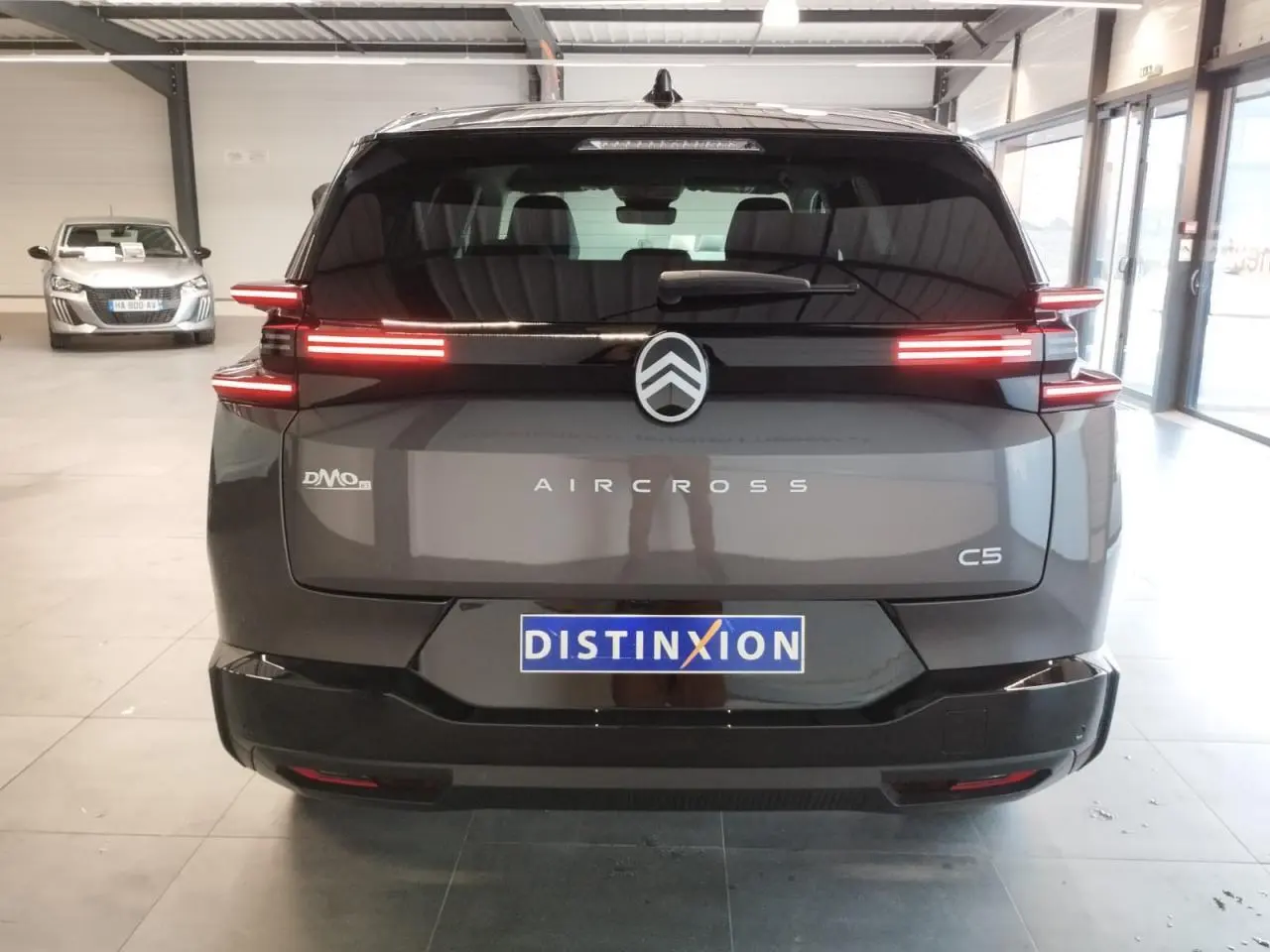 Vue arrière d'un Citroën C5 Aircross gris platine avec feux arrière LED distinctifs allumés en intérieur showroom.
