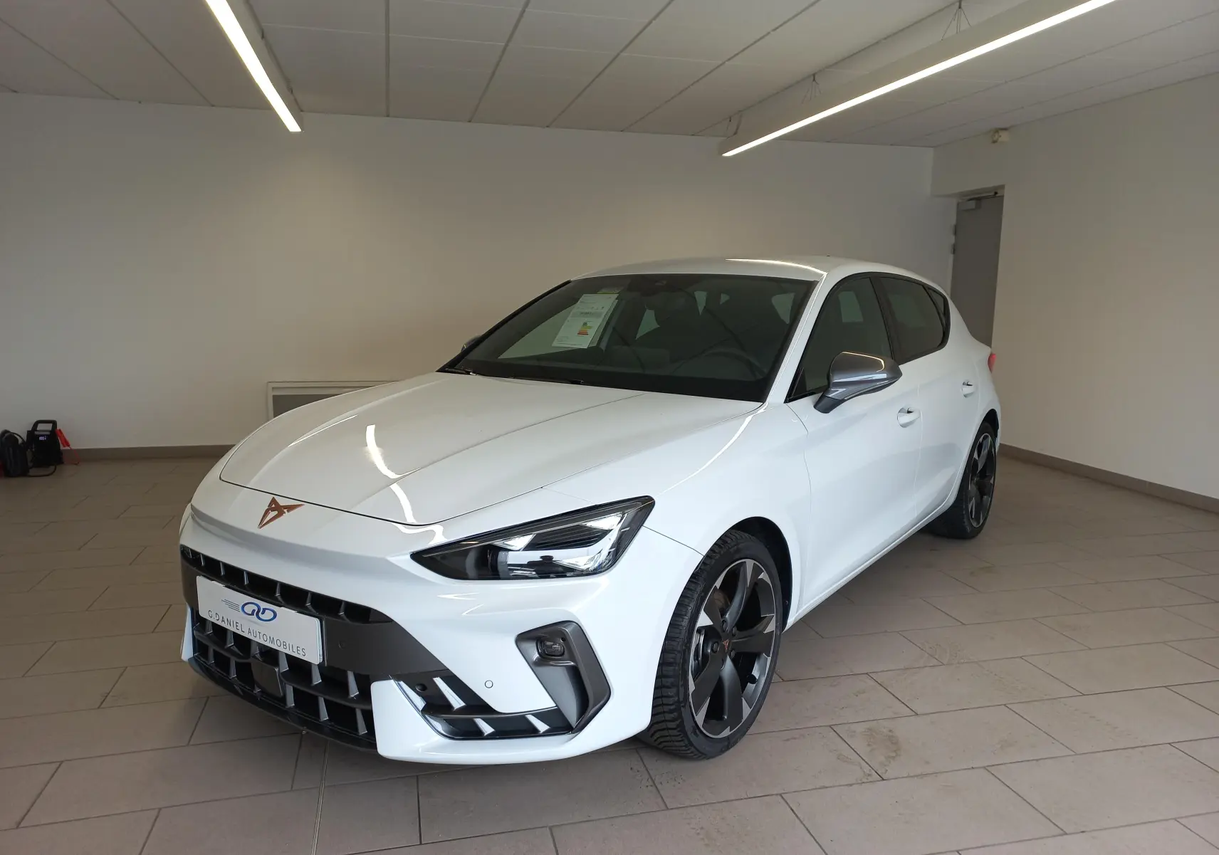 Vue 3/4 avant d'une CUPRA Leon blanche Nevada métallisée, avec jantes noires et logo CUPRA cuivré sur le capot.