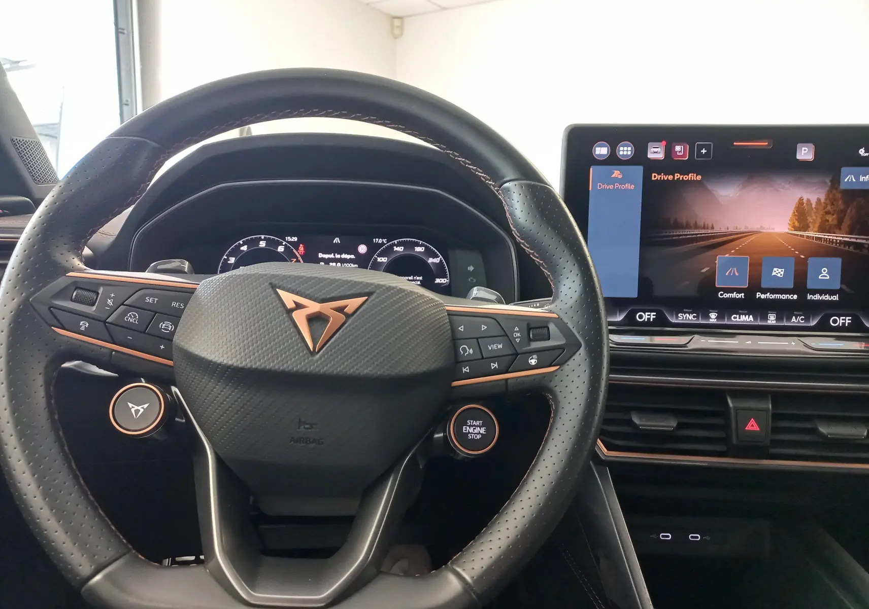 Vue intérieure centrée sur le volant noir perforé avec logo CUPRA cuivré et écran tactile du tableau de bord.