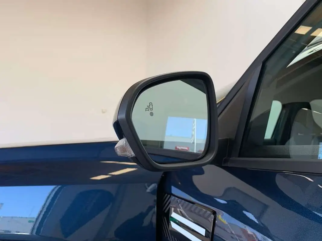 Rétroviseur côté gauche du Dacia Bigster bleu indigo avec toit noir, montrant le détecteur d'angle mort intégré.