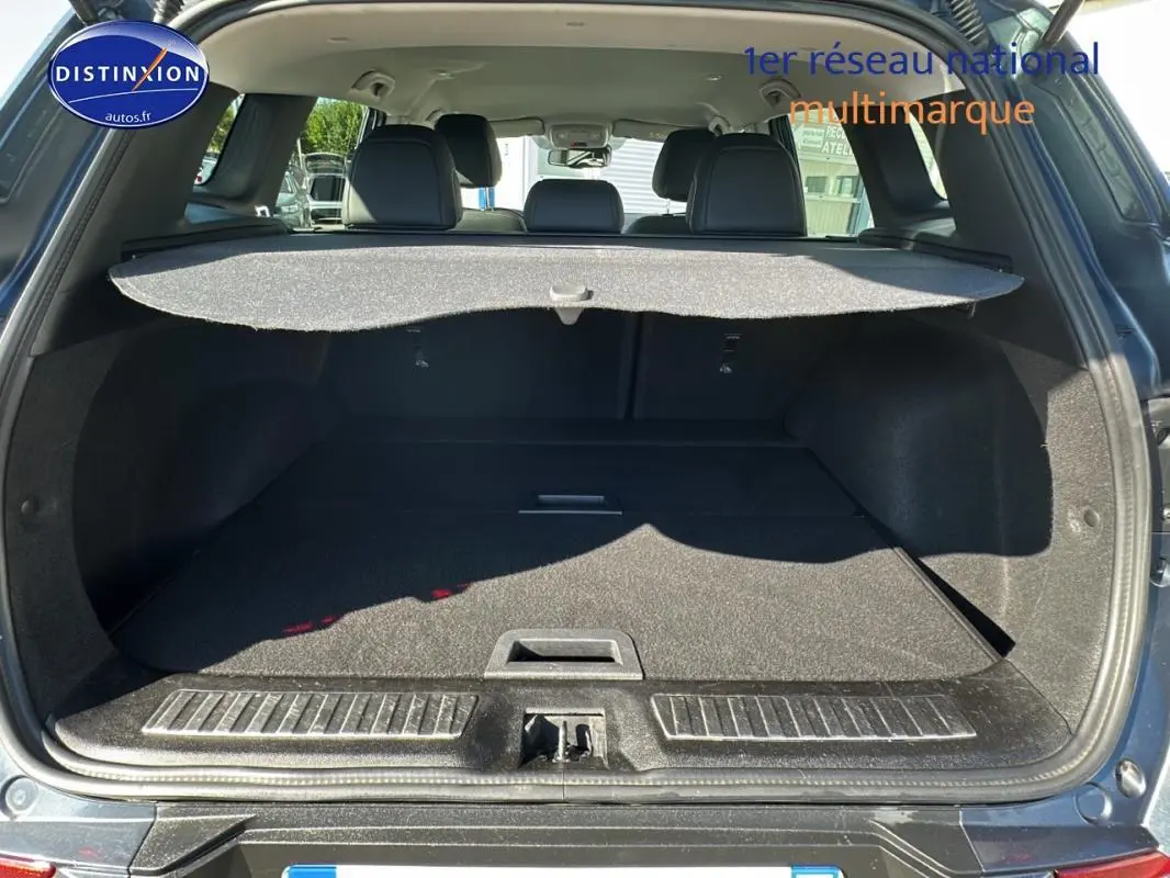 Coffre ouvert vu de l'arrière d'un Renault Kadjar gris foncé avec cache-bagages et sièges arrière noirs visibles.