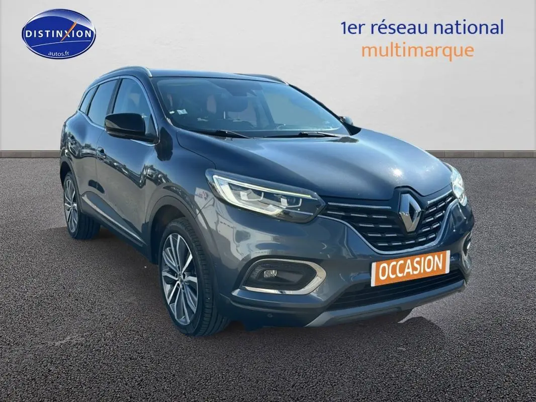 Renault Kadjar gris foncé en 3/4 avant droit avec jantes alliage 19 pouces et barres de toit visibles.