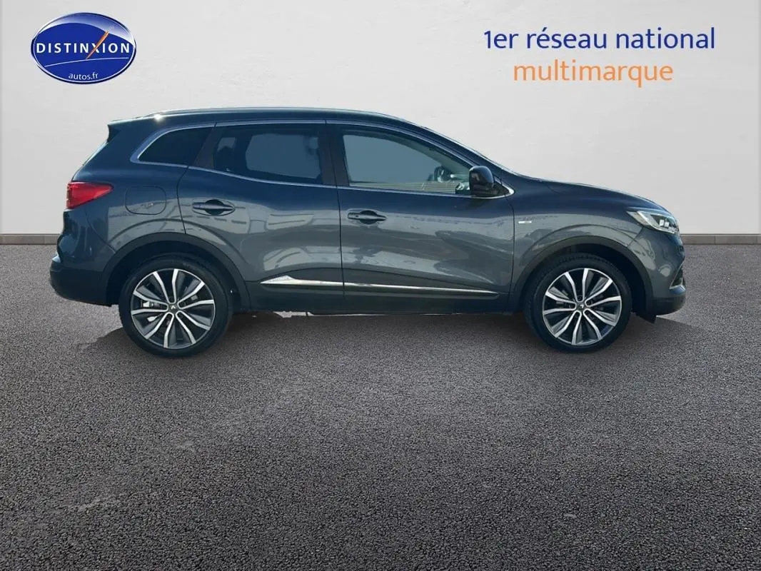 Profil côté droit du Renault Kadjar gris foncé 2019 avec jantes alliage 19 pouces et barres de toit visibles.