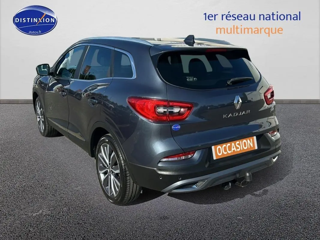 Vue 3/4 arrière gauche d'un Renault Kadjar gris foncé avec jantes alliage 19 pouces et barres de toit visibles.