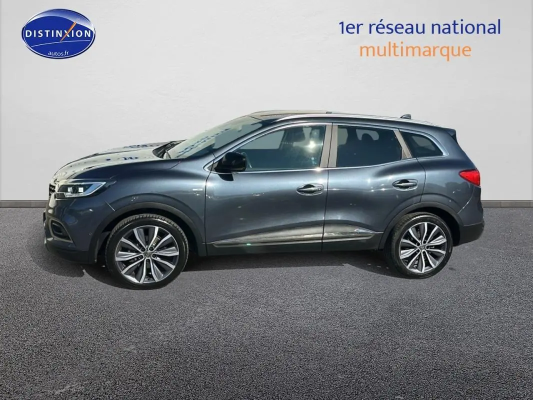 Renault Kadjar gris foncé vu de profil côté gauche avec jantes alliage 19 pouces et barres de toit visibles.