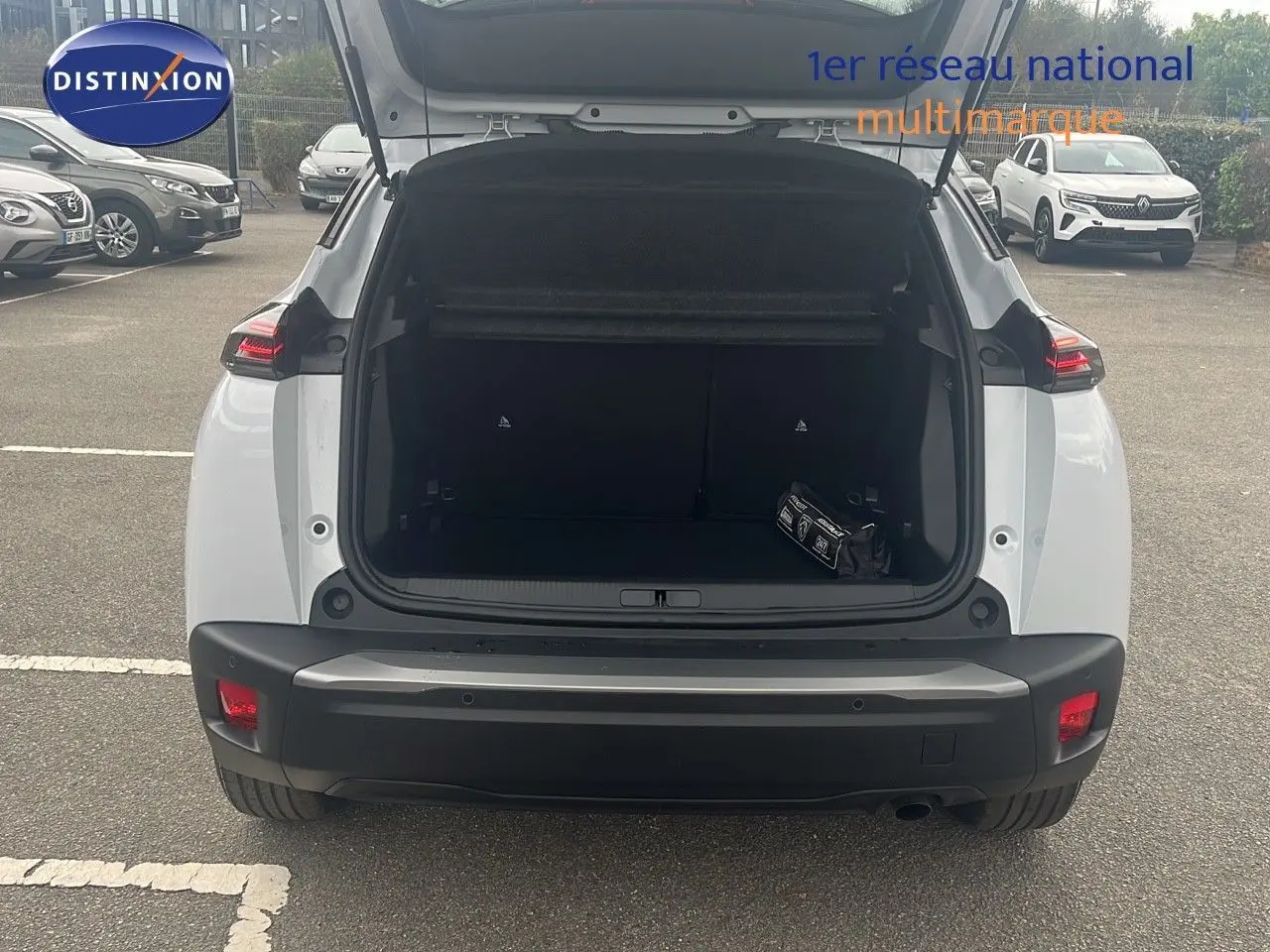 Vue arrière d'un Peugeot 2008 blanc Okenite Metal avec coffre ouvert montrant un kit de sécurité à l'intérieur.
