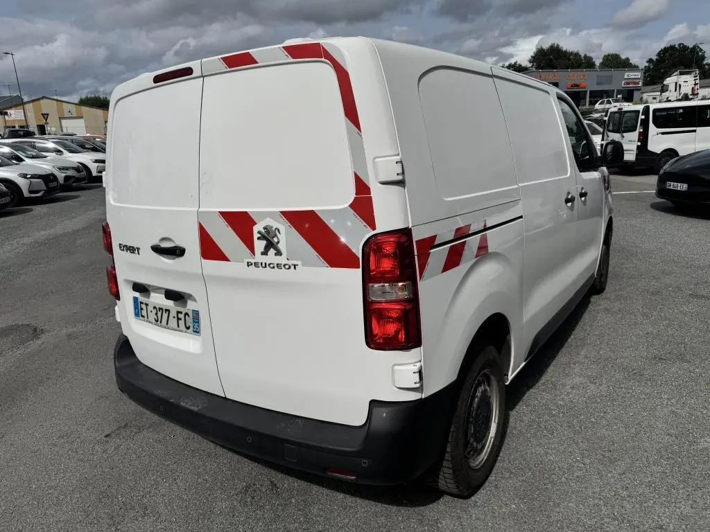 Vue 3/4 arrière droite du Peugeot Expert Fourgon blanc avec bandes réfléchissantes rouges et blanches sur portes et flanc.
