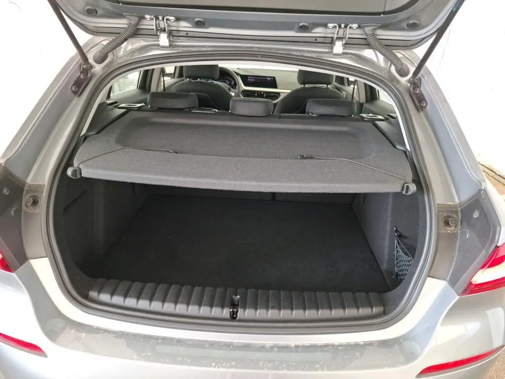 Coffre ouvert vu de l'arrière d'une BMW Série 1 116d gris 2022, avec cache-bagages et intérieur visible.