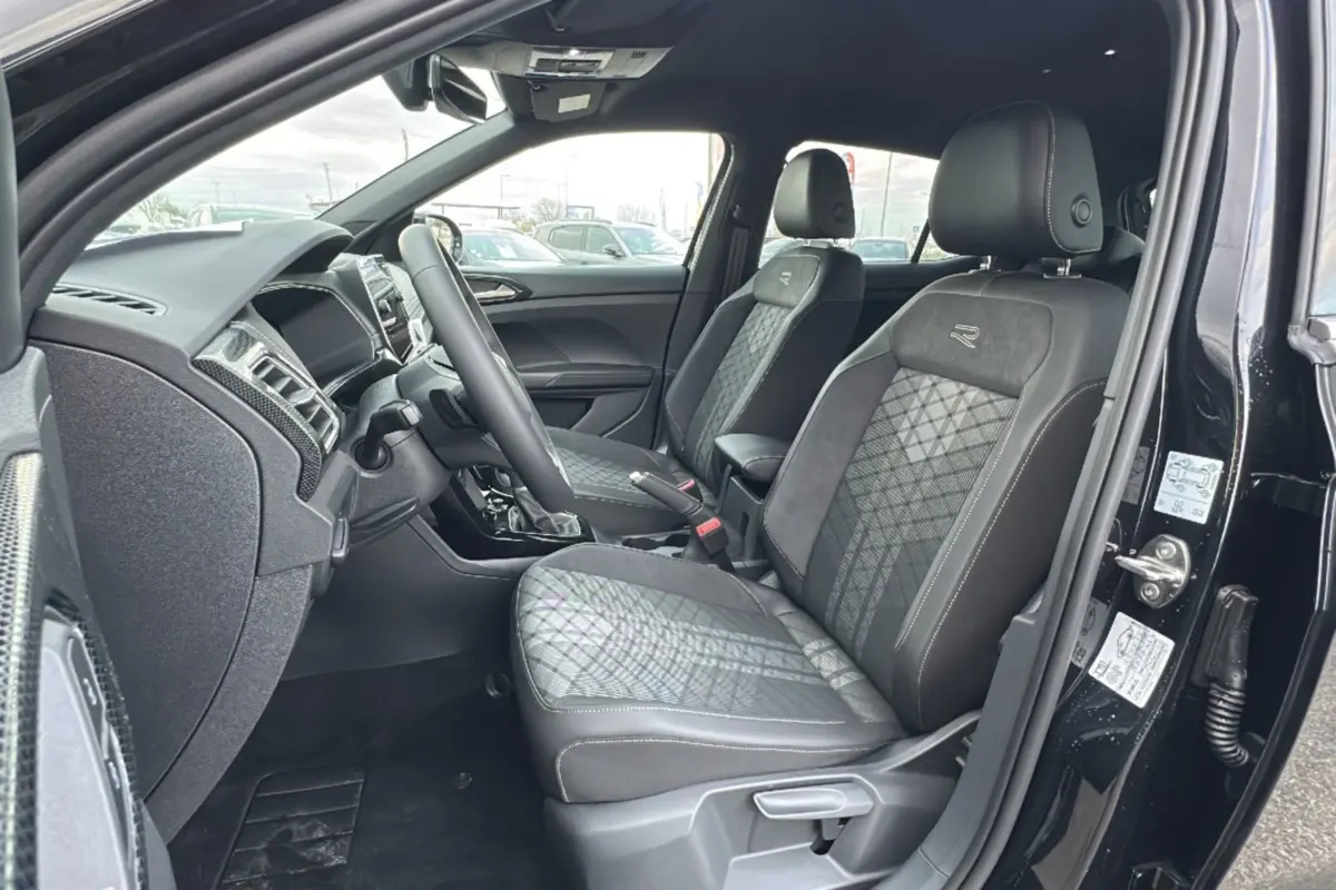 Vue intérieure côté conducteur du Volkswagen T-Cross noir intense 2025, sièges R-Line en tissu et alcantara avec surpiqûres contrastées.