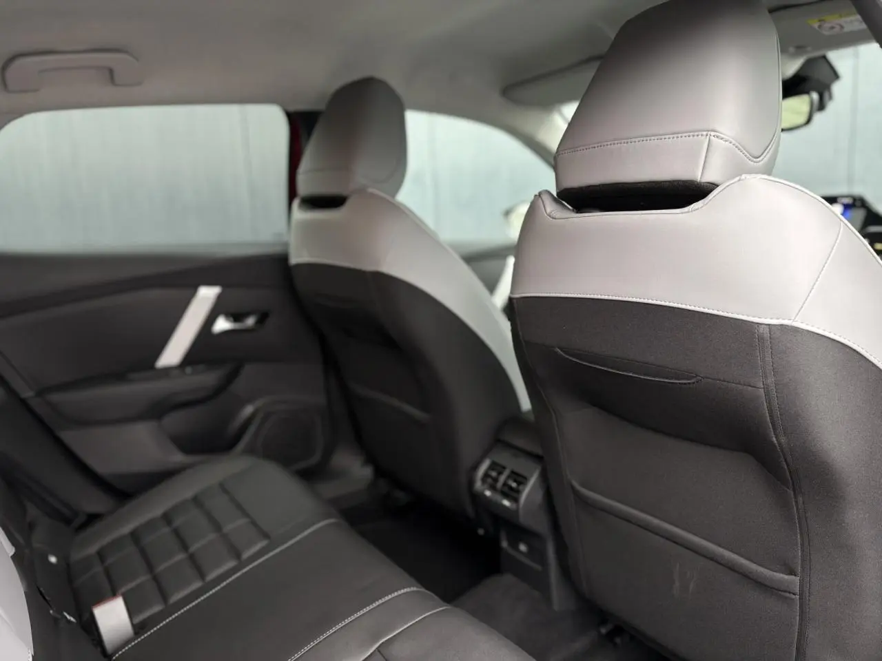 Vue intérieure arrière de la Citroën C4 Hybrid 2025 montrant les sièges bicolores gris clair et noir avec aérations centrales.
