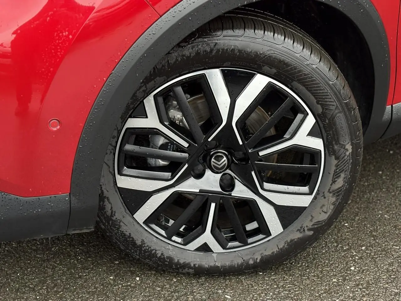 Gros plan sur la roue avant gauche de la Citroën C4 Hybrid 2025 en Rouge Elixir avec jante alliage 18 pouces diamantée.