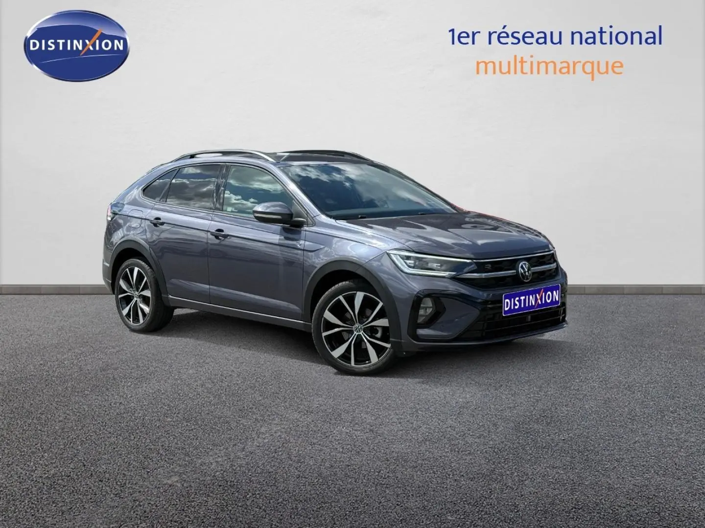 Volkswagen Taigo gris Ascot en 3/4 avant droit avec jantes alliage et barres de toit visibles.