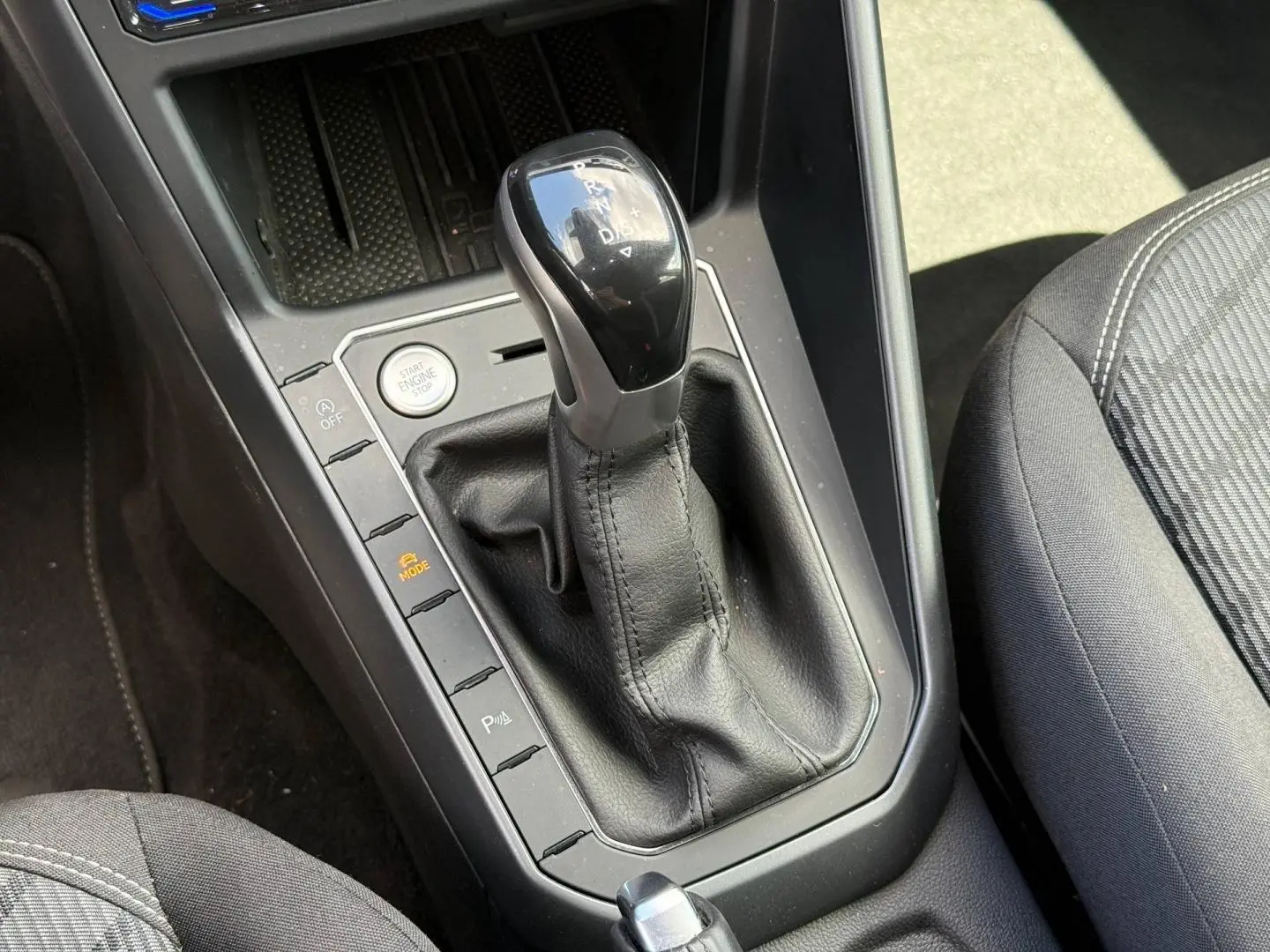 Gros plan sur le levier de vitesses automatique noir et gris du Volkswagen Taigo 1.0 TSI R-Line, avec siège tissu gris visible.