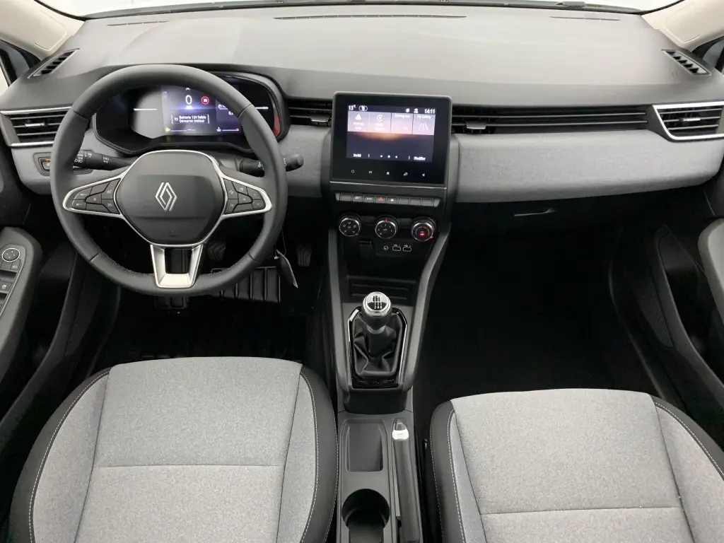 Vue intérieure avant de la Renault Clio V TCE 90 avec tableau de bord noir, volant multifonction et sellerie textile grise.